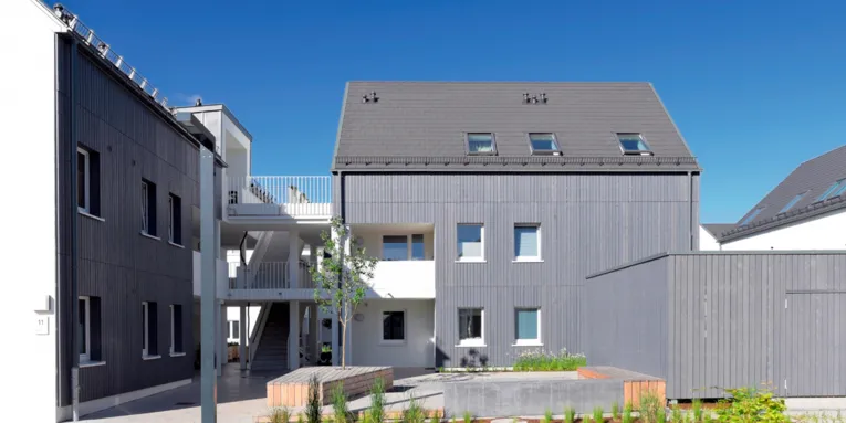Blick von außen auf ein modernes Gebäude mit Holzfassade und mehreren Wohneinheiten.